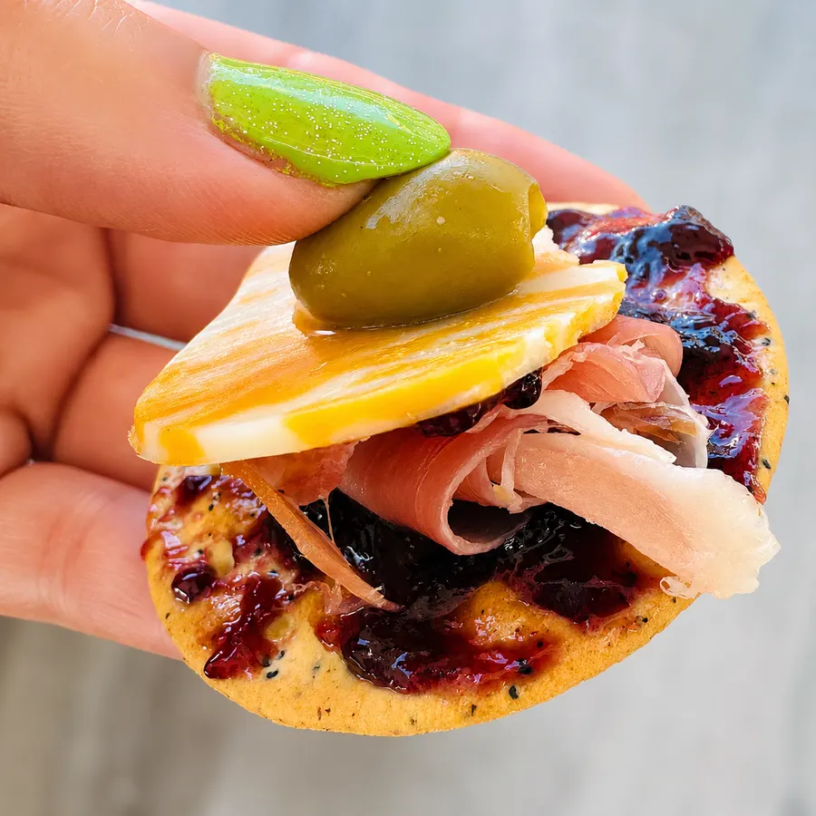 The perfect bite: cracker with jam, prosciutto, cheese and an olive